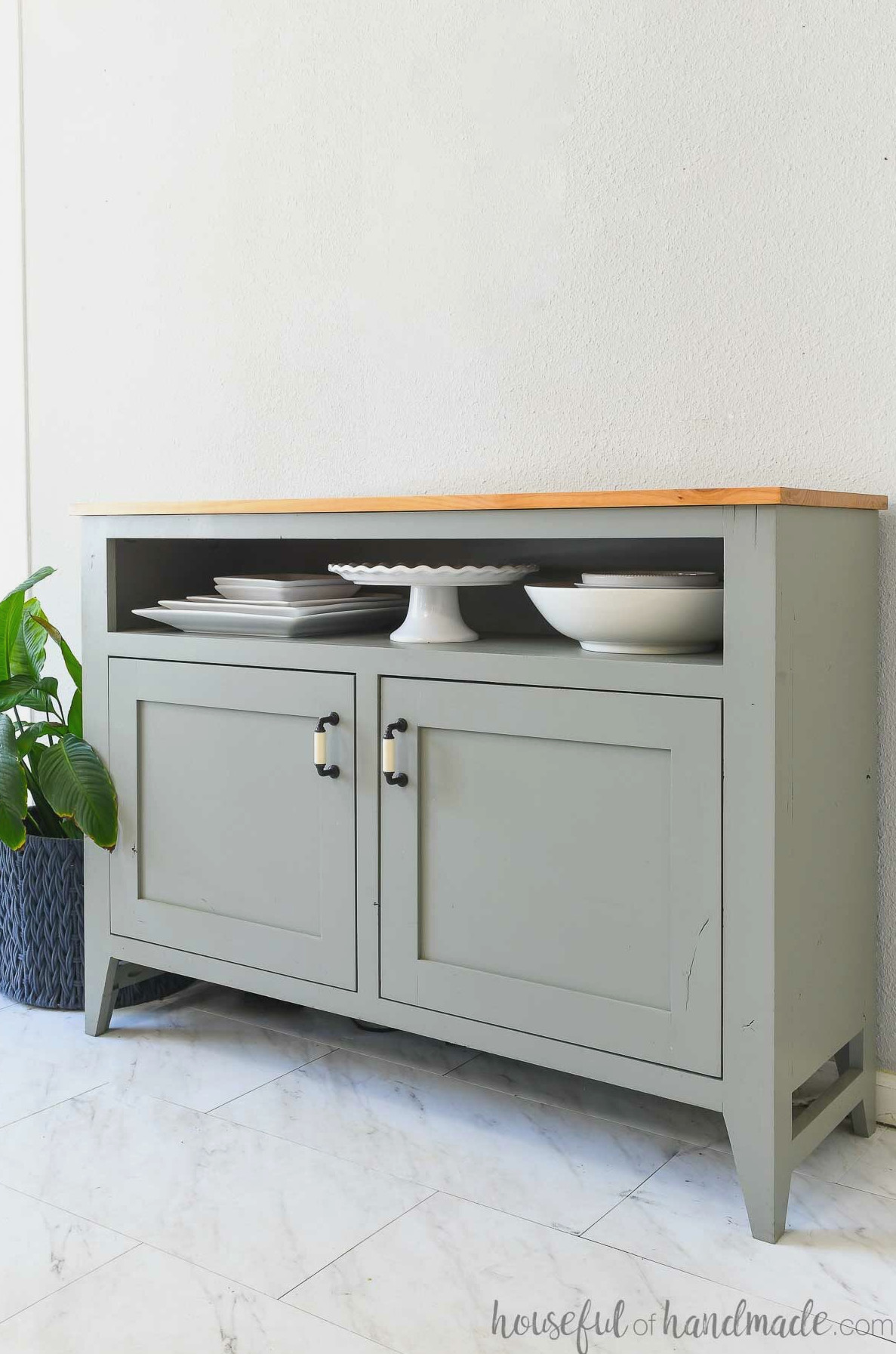 4' sideboard with serving dish shelf with a peace lily next to it.