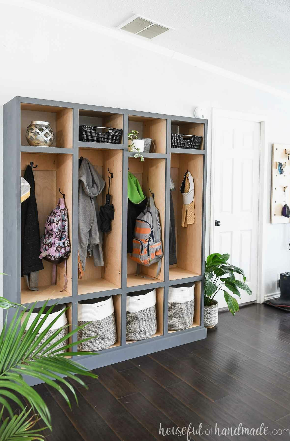 DIY mudroom storage lockers with natural wood tone on the inside and gray-blue painted outside in an entryway filled with coats and backpacks.