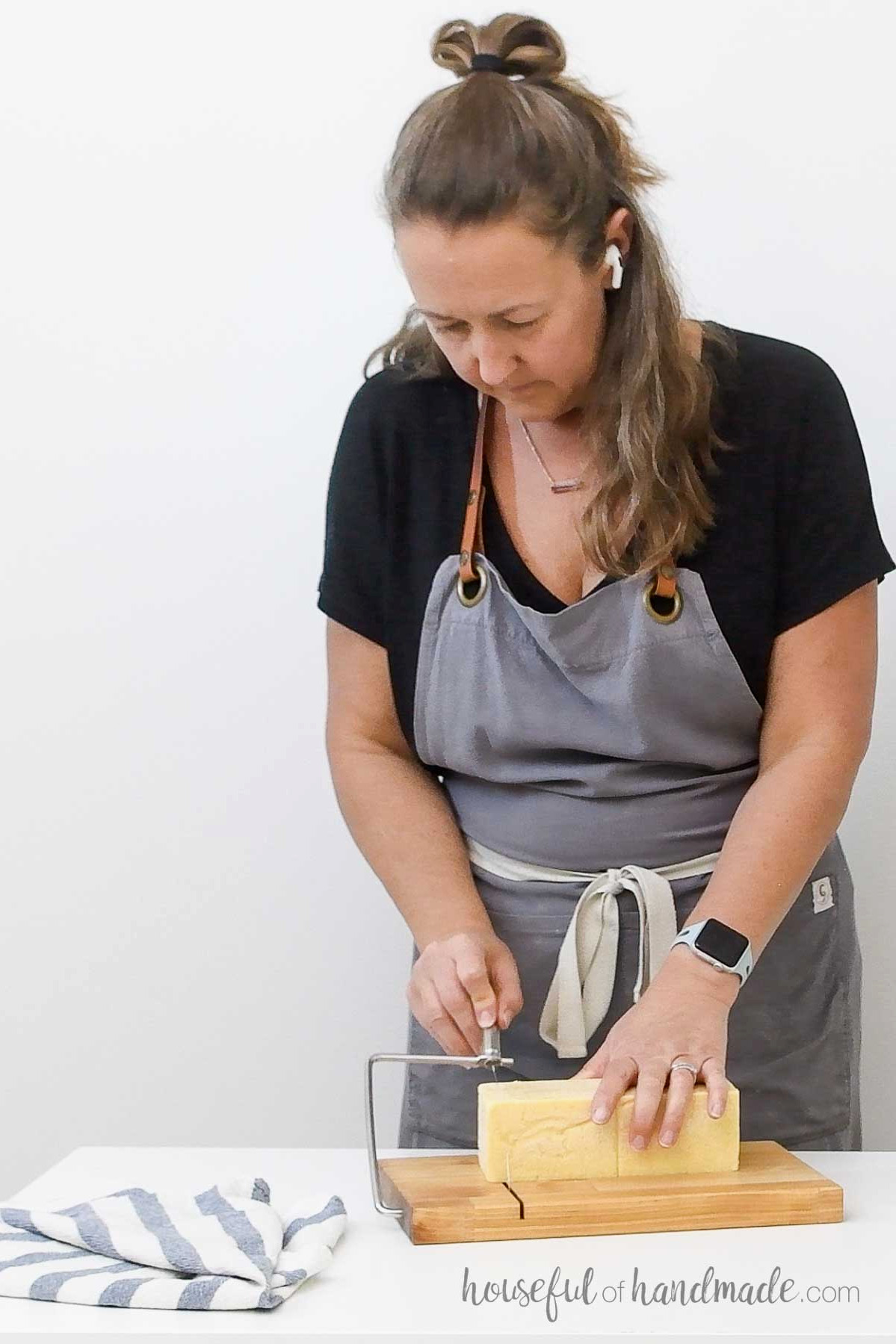 Woman cutting cheese on a wooden cheese slicer.