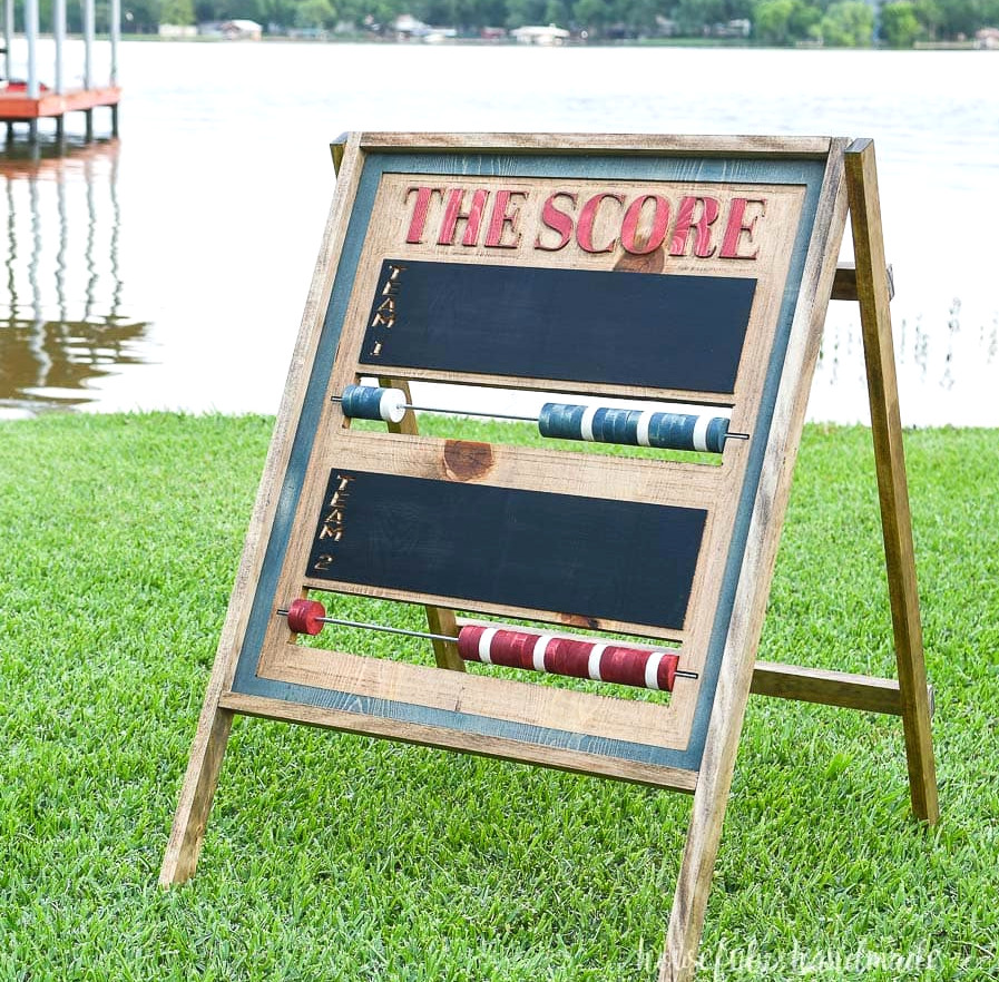 Square image of a carved scoreboard on the grass with red and blue wooden scoring beads.