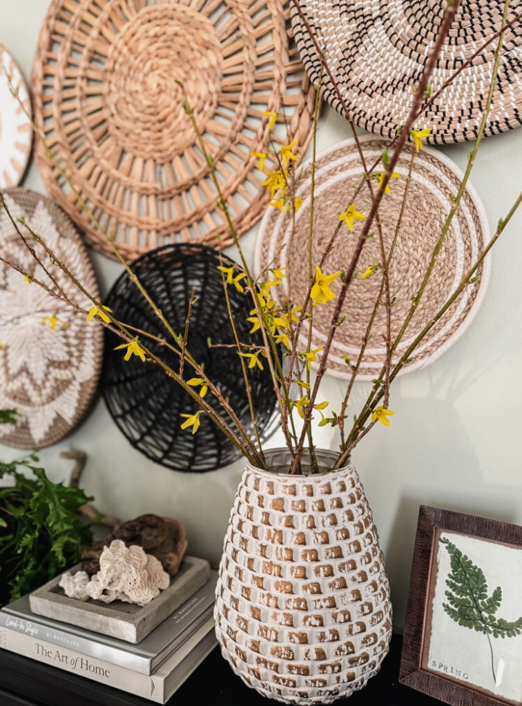 forsythia in vase with basket wall behind it